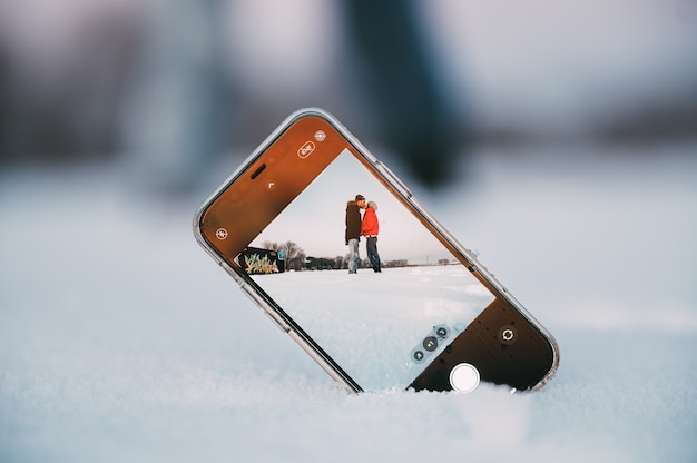 Coppia di innamorati che si abbracciano tenendo selfie sul cellulare posizionato sulla neve in campagna