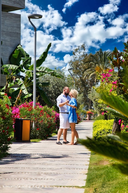 Loving couple enjoying honeymoon in luxury hotel, walking through grounds with palm trees and beauty flowers. Happy lovers on romantic trip have fun on summer vacation. Concept romance and relaxation