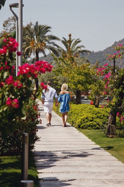 Loving couple enjoying honeymoon in luxury hotel, walking through grounds with palm trees and beauty flowers