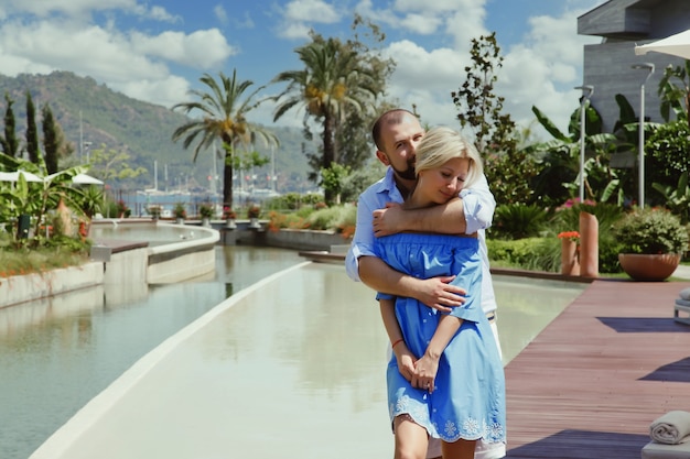 Влюбленная пара наслаждается медовым месяцем в роскошном отеле, гуляя по территории с пальмами и бассейном. Счастливые влюбленные в романтическом путешествии весело проводят время на летних каникулах. Понятие романтики и релаксации