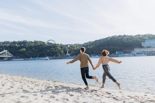 愛するカップルは、お互いに抱き合って笑い、暖かい夏の夜を楽しんでいます。ロマンチックなカップルがビーチを走っています。