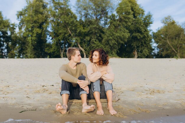 愛するカップルは、お互いに抱き合って笑い、暖かい夏の夜を楽しんでいます海のそばに座っているロマンチックなカップル男と女はお互いを見ています