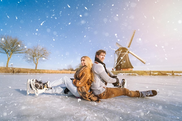 Loving couple having fun on ice in typical dutch landscape with windmill woman and man ice skating