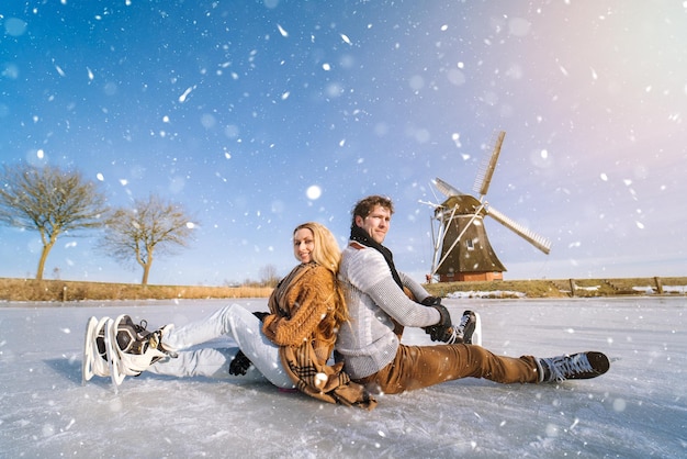 Loving couple having fun on ice in typical dutch landscape with windmill woman and man ice skating