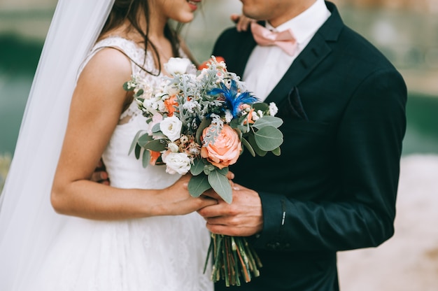 Loving couple holding hands with rings and bouquet against wedding dress