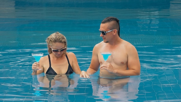 Photo the loving couple hugs and kisses drinking blue cocktail alcohol liquor in swimming pool at hotel outdoor portrait of caucasian man and woman