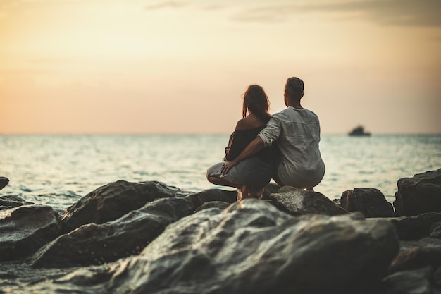 A loving couple is having fun and hugging on the empty sandy sea beach at sunset.They are looking away.