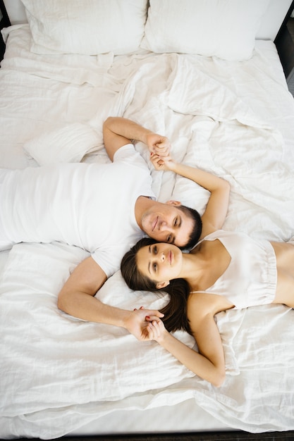 Loving couple lying in a white bed. Man and woman hugging