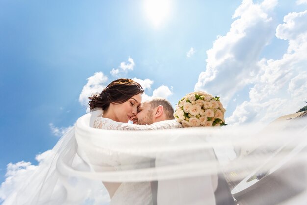 Loving couple of newlyweds walks in the city and a veil flying in the wind on blue sky background