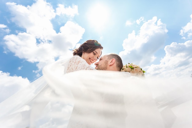 Loving couple of newlyweds walks in the city with a bouquet of roses and a veil flying in the wind