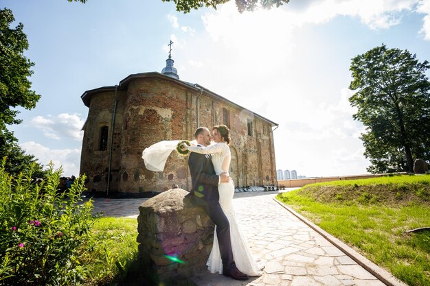 Loving couple of newlyweds walks near ancient old church in summer sunny day