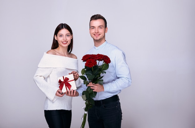 Coppia di innamorati in posa con un regalo e rose rosse, sorridenti.