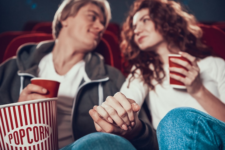 Photo loving couple sit holding hands in cinema.