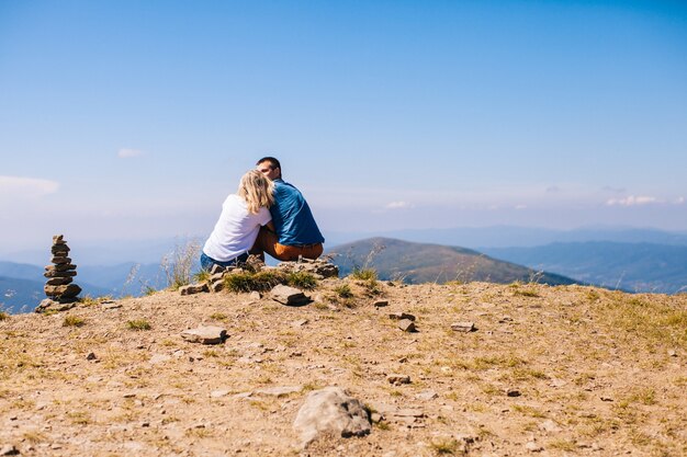 A loving couple sits on a hillside and admiring the view in the mountains