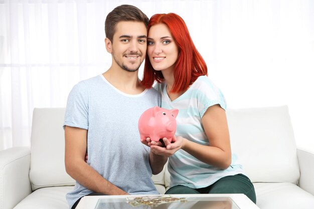 Loving couple sitting in sofa with piggy bank in room