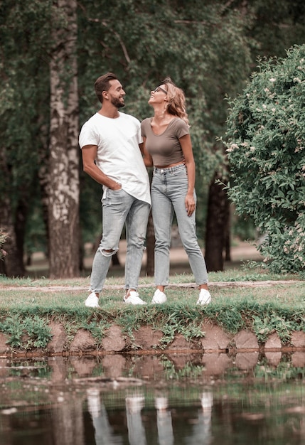 Влюбленная пара стоит на траве у озера в парке