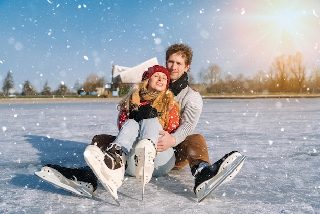 Loving couple in warm sweaters having fun on ice woman and man\
ice skating outdoors in sunny snowy