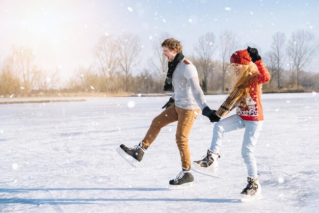 Coppia di innamorati in maglioni caldi che si divertono sul ghiaccio donna e uomo che pattinano sul ghiaccio all'aperto nella neve soleggiata