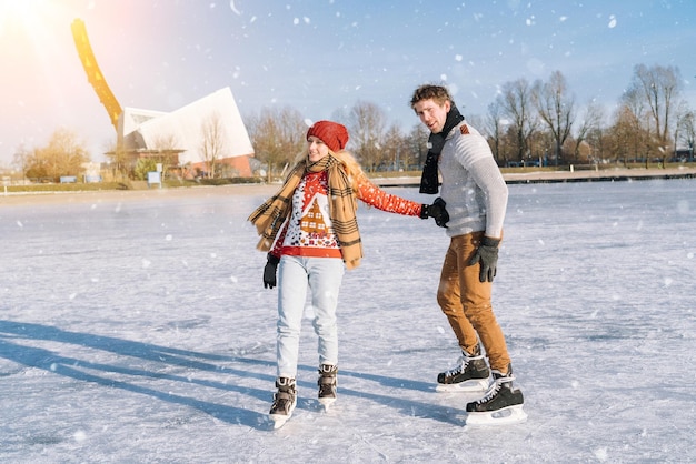 Loving couple in warm sweaters having fun on ice woman and man ice skating outdoors in sunny snowy