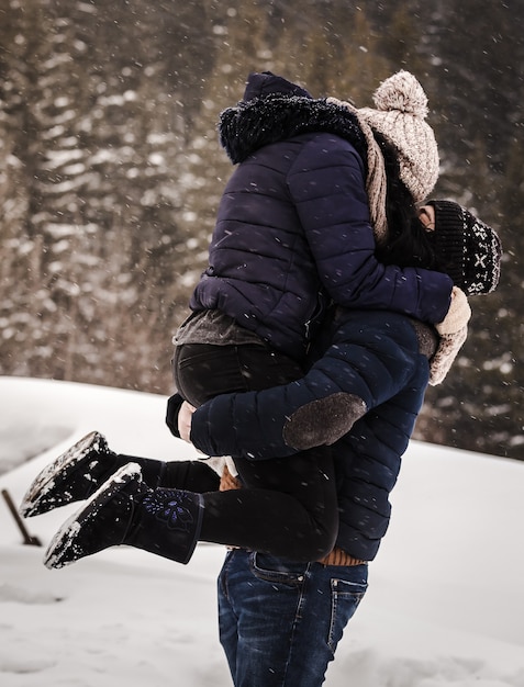 소나무 숲의 배경에 눈이 내리는 동안 겨울 옷을 입은 사랑하는 부부