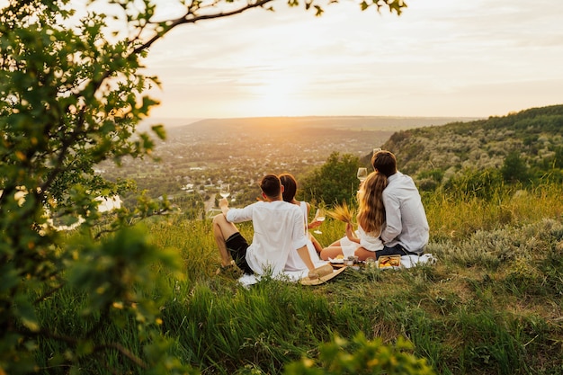 Loving couples drinking wine in summer day on mountain during sunset.