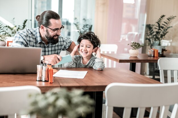 Loving dad. Cute laughing dark-haired son speaking with his caring loving dad sitting in cafeteria