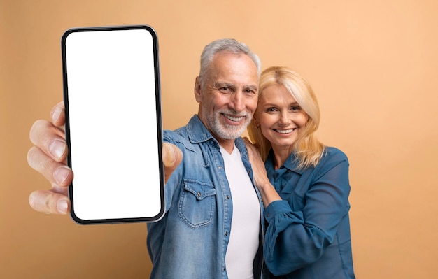 Loving elderly couple showing phone with white blank screen