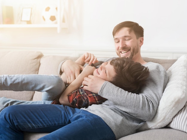 Loving father having fun and tickling his son on sofa at home