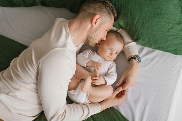 A loving father lies on the bed with his baby son and hugs him