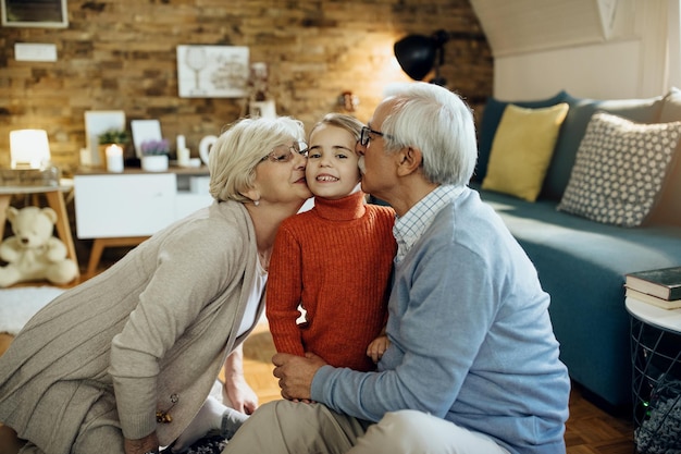 Loving grandparents kissing their granddaughter while spending time together at home