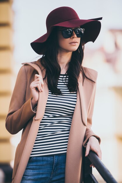 Loving her style. Beautiful young woman in sunglasses looking away while leaning to fence outdoors