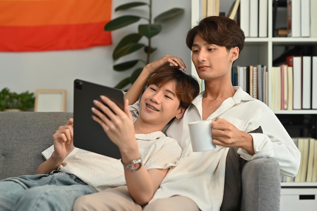 Loving homosexual couple embracing and using digital tablet on couch LGBT love and lifestyle relationship concept