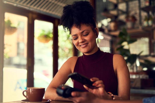 Loving how easy it is to pay Cropped shot of a young woman paying using NFC technology in a cafe