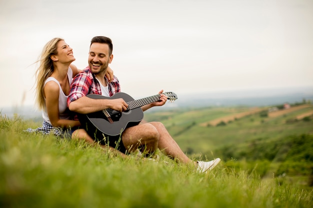 Amare uomo seduto sull'erba con la sua ragazza e suonare la chitarra