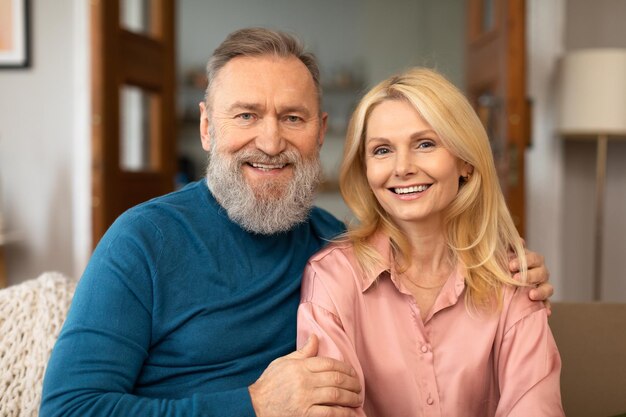 Loving mature spouses hugging sitting on couch at home portrait