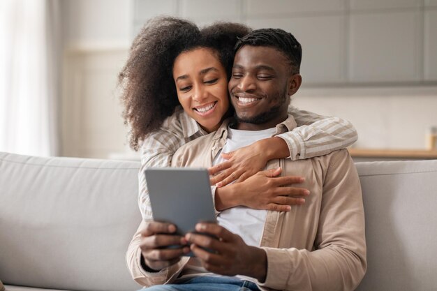 Loving millennial african american couple enjoys websurfing on tablet indoors