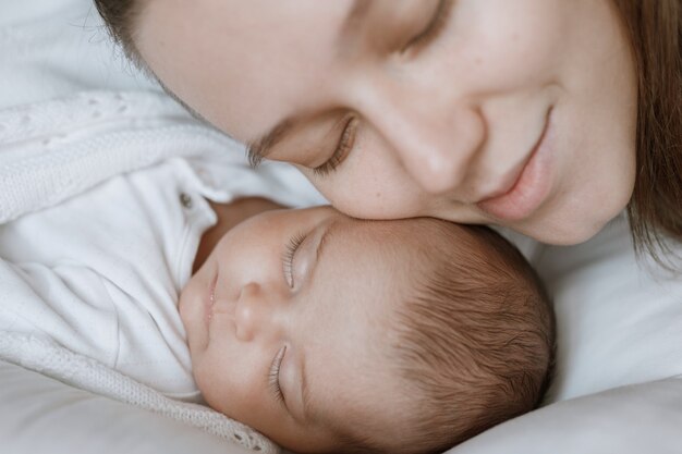 loving mom carying of her newborn baby at home Baby is resting in bed