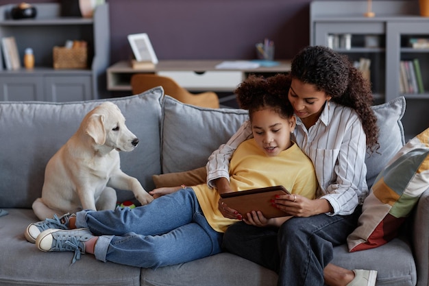 Любящая мать и дочь с помощью цифрового планшета вместе с милой собакой
