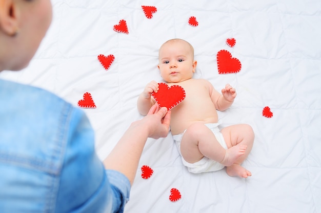 사랑하는 어머니는 하트 세트에 누워 있는 아기 아들에게 발렌타인 하트를 줍니다.