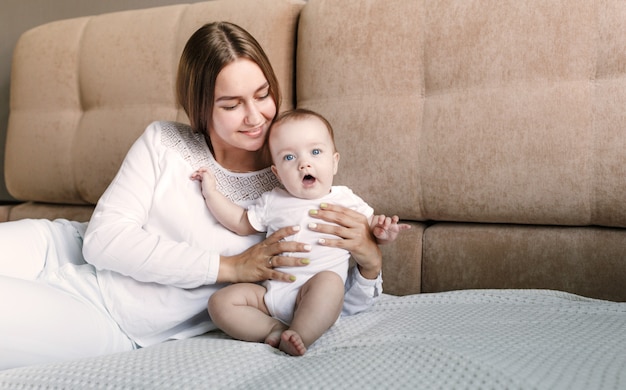 A loving mother and her little daughter. Young mother plays with her little beloved daughter on the couch.