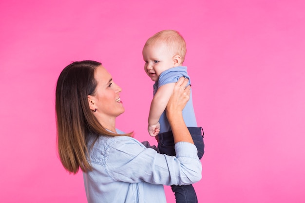 Loving mother playing with her baby boy on pink.