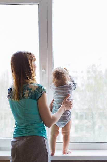 Foto madre amorevole che gioca con suo figlio vicino a una finestra.