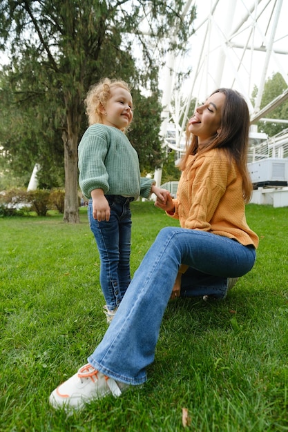 Loving mother walks with her cute daughter in the park posing\
mom sticks out her tongue daughter smiles loving family