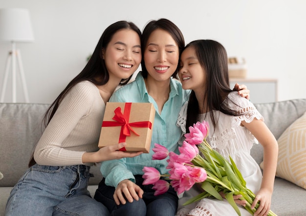 Photo loving multi generation asian family with tulips and gift box hugging with closed eyes celebrating