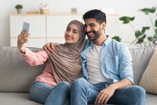 Loving muslim spouses making selfie on phone posing at home