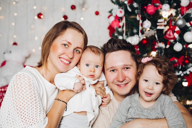 Genitori amorosi con i bambini a natale all'albero di abete decorato.