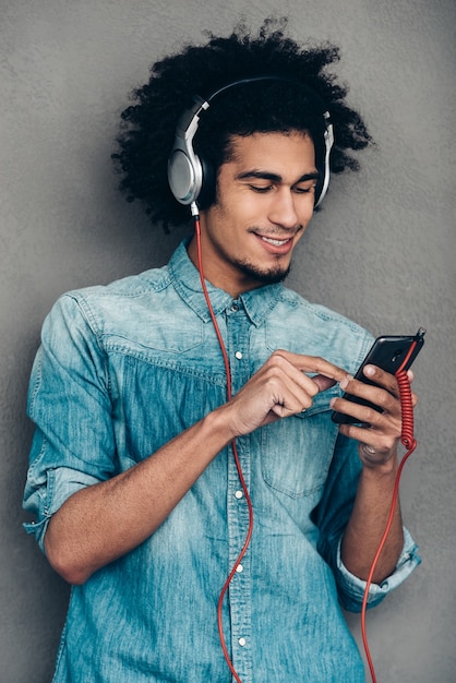 Loving that song. Cheerful young African man wearing headphones and using smartphone 