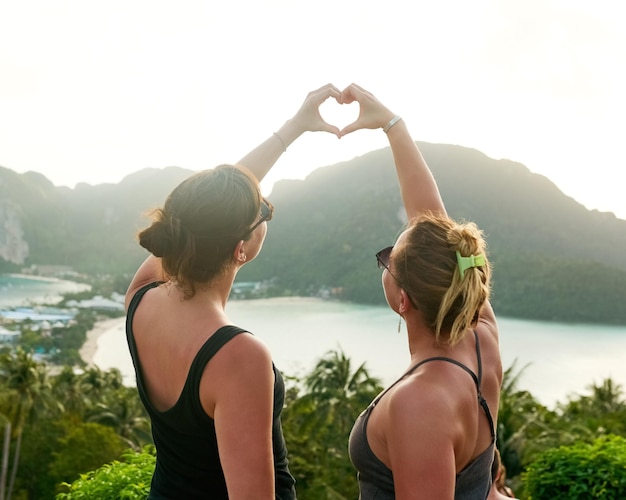 Loving their vacay Shot of two friends making a heart shape with their hands while on holiday in Thailand