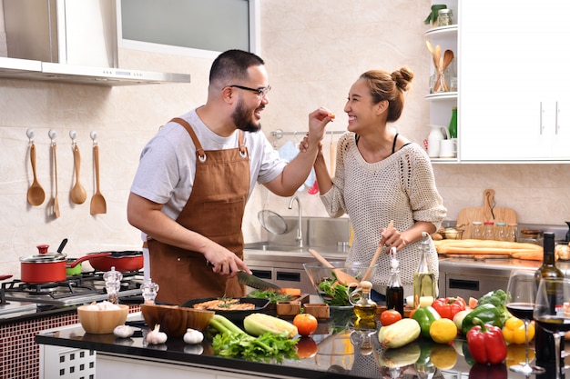 Giovani coppie asiatiche amorose che cucinano nella cucina che produce insieme alimento sano sentirsi divertimento