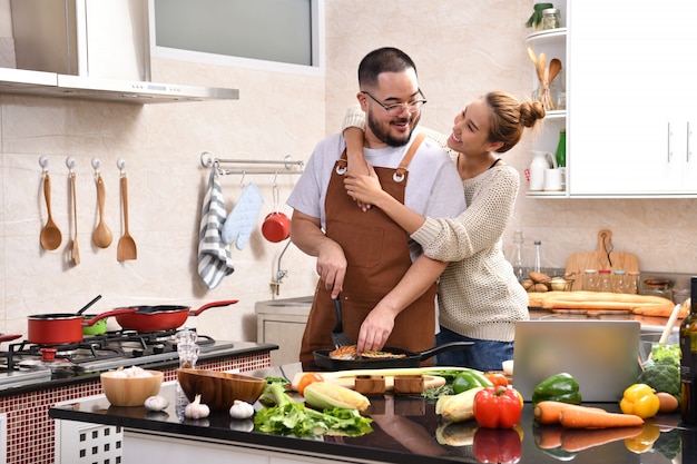 Loving young Asian couple cooking in kitchen making healthy food together feeling fun